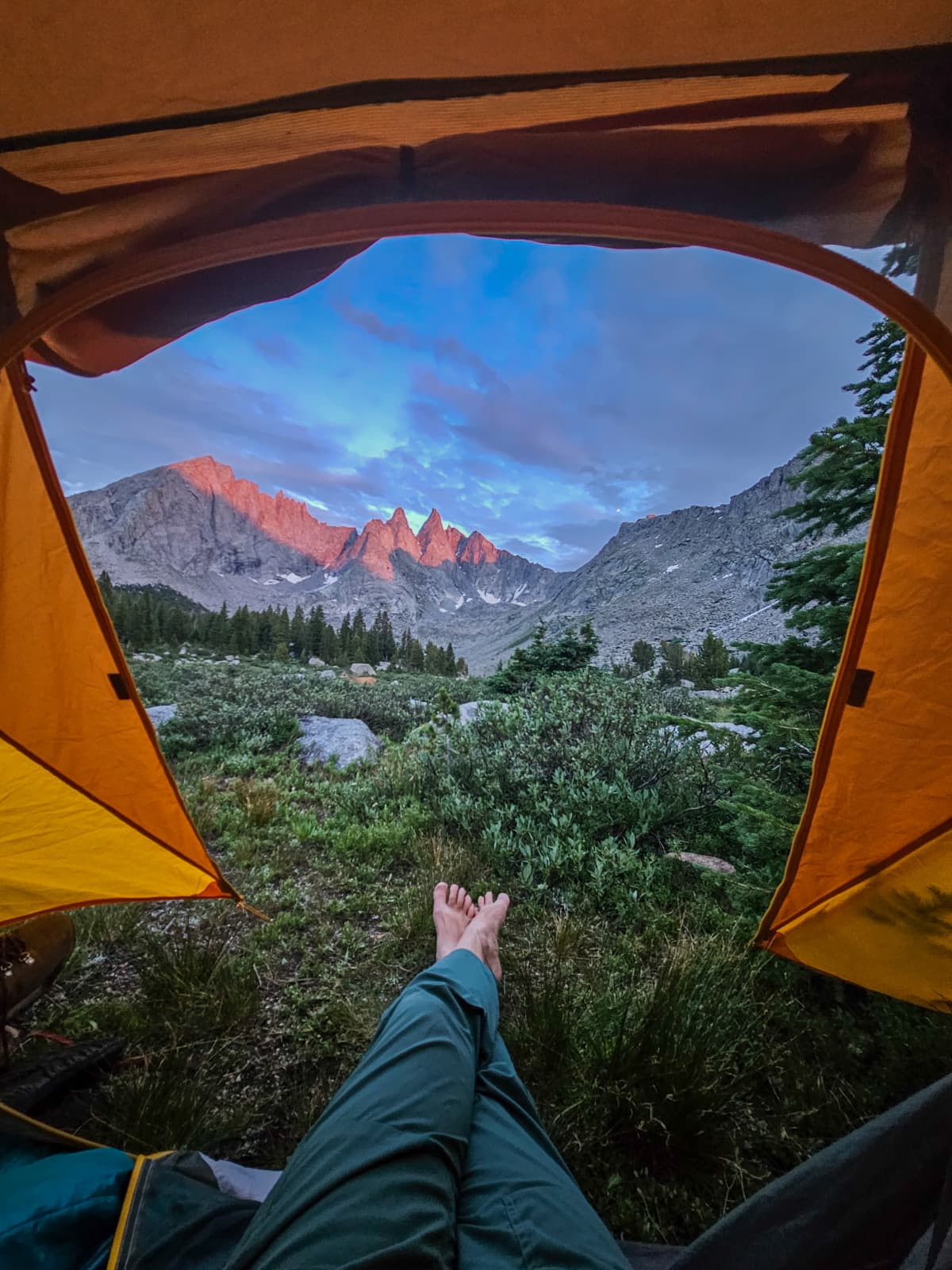 Woman's outstretched legs in a tent while looking at the backside of the Cirque of the Towers mountains in the Wind River range of Wyoming