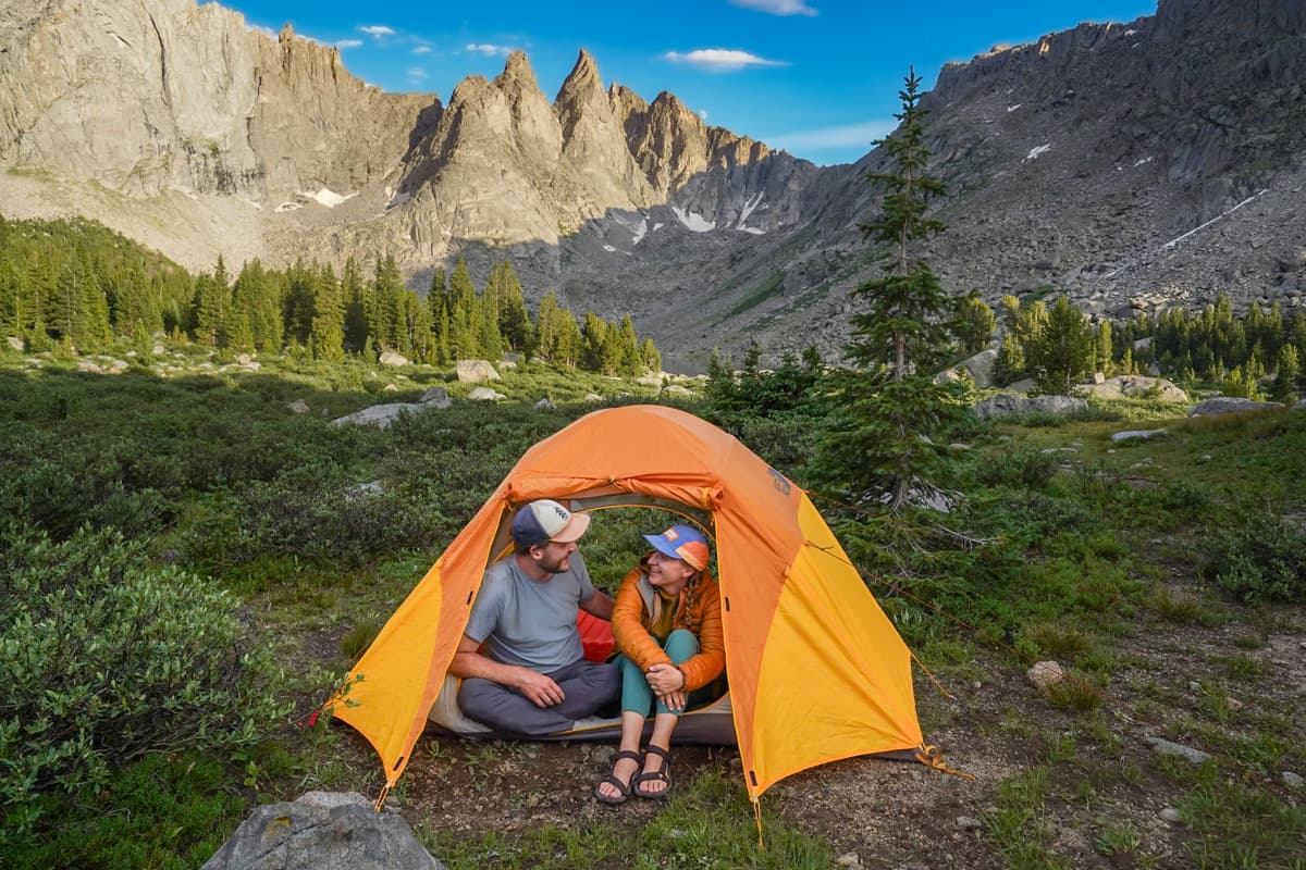 Couple sitting in a tent with the Cirque of the Towers mountain range in the background in the Wind River mountains of Wyoming