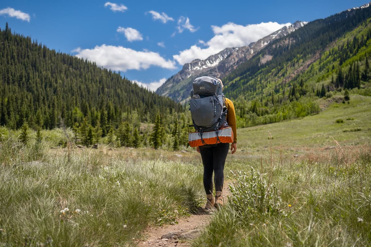 Woman wearing a backpacking backpac with Rocky Mountains in the background along the Conundrum Hot Springs Trail in Maroon Bells-Snowmass Wilderness in Aspen, Colorado