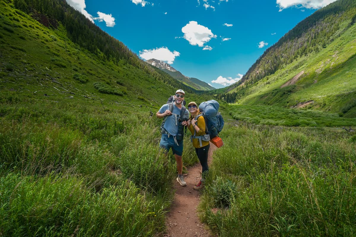 Couple with backpacking gear at the Conundrum Hot Springs trailhead with mountains in the background in Maroon Bells-Snowmass Wilderness in Aspen, Colorado