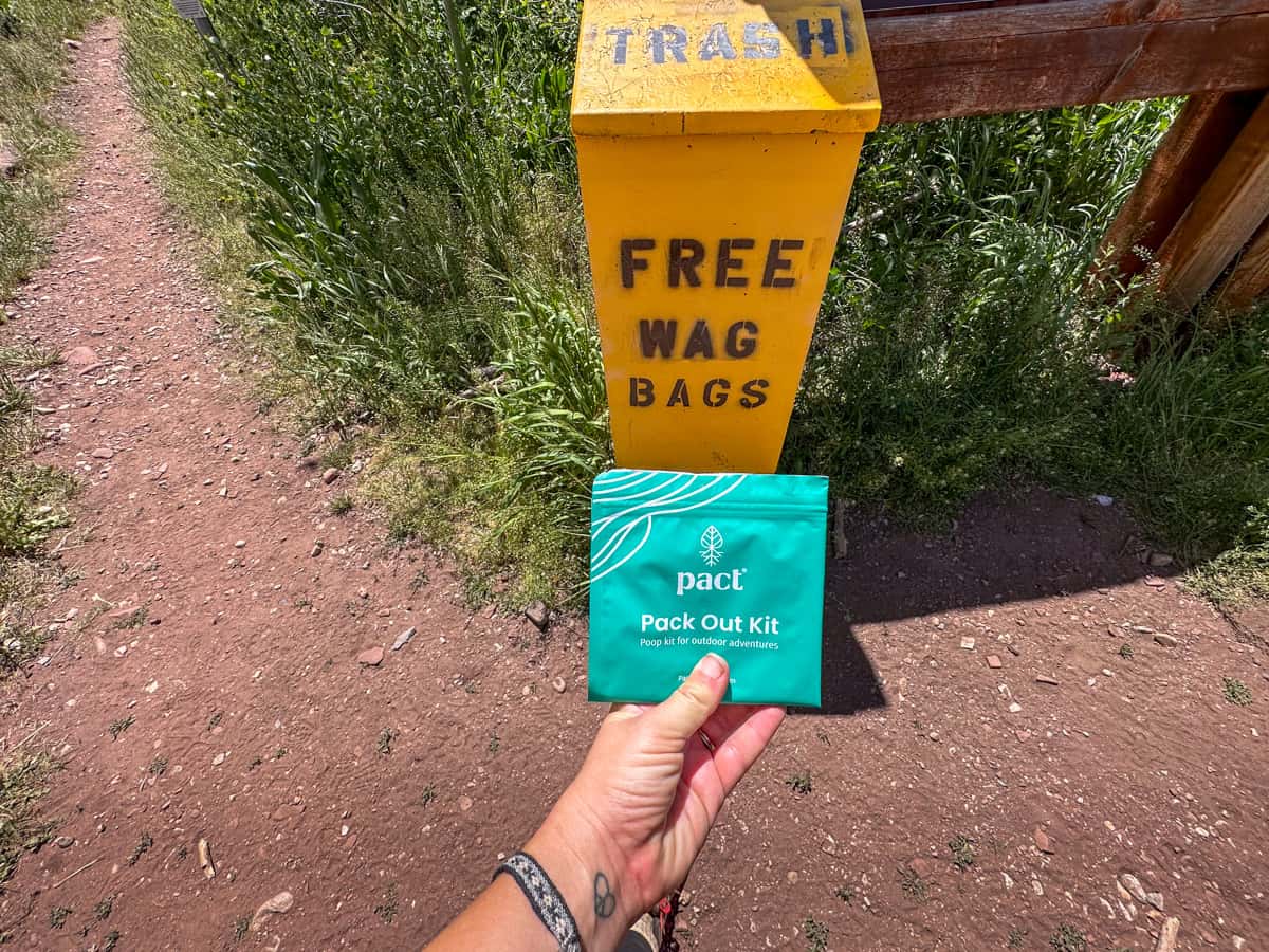Woman holding a wag bag in front of free wag bag receptacle at the Conundrum Hot Springs trailhead in Maroon Bells-Snowmass Wilderness in Aspen, Colorado