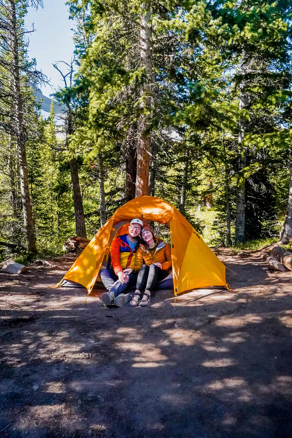 Couple sitting in a tent with pine trees and a mountain in the background along the Conundrum Hot Springs Trail in Maroon Bells-Snowmass Wilderness in Aspen, Colorado