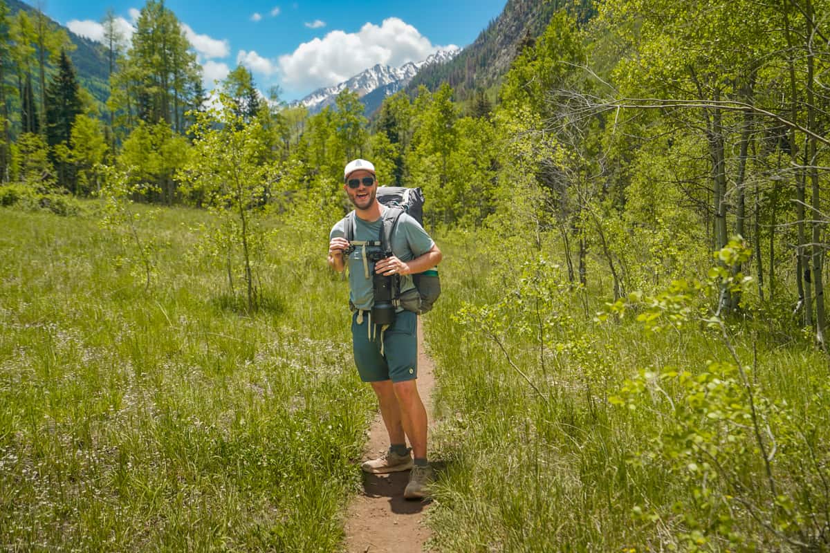 Man with a backpacking back hiking along the Conundrum Hot Springs trail with snowcapped mountains in the background in Maroon Bells-Snowmass Wilderness in Aspen, Colorado