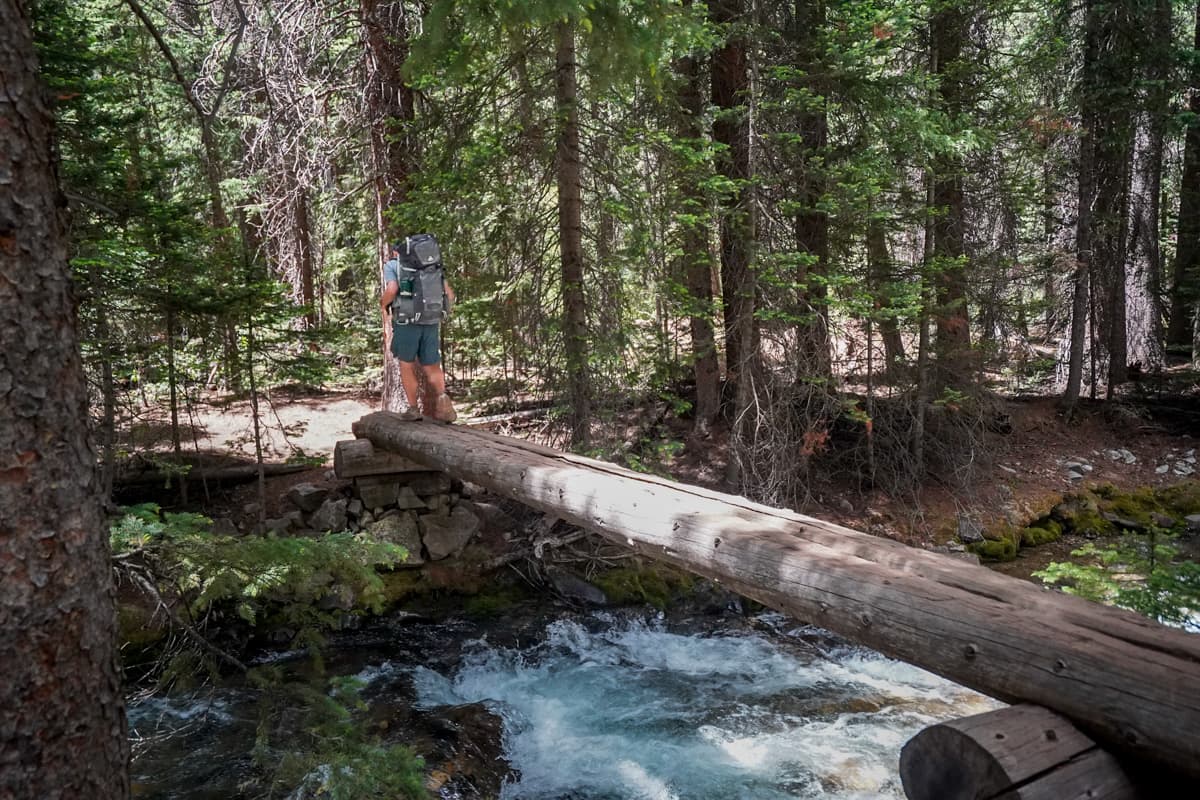 Man walking on a log bridge across Conundrum Creek along the Conundrum Hot Springs Trail in Maroon Bells-Snowmass Wilderness in Aspen, Colorado