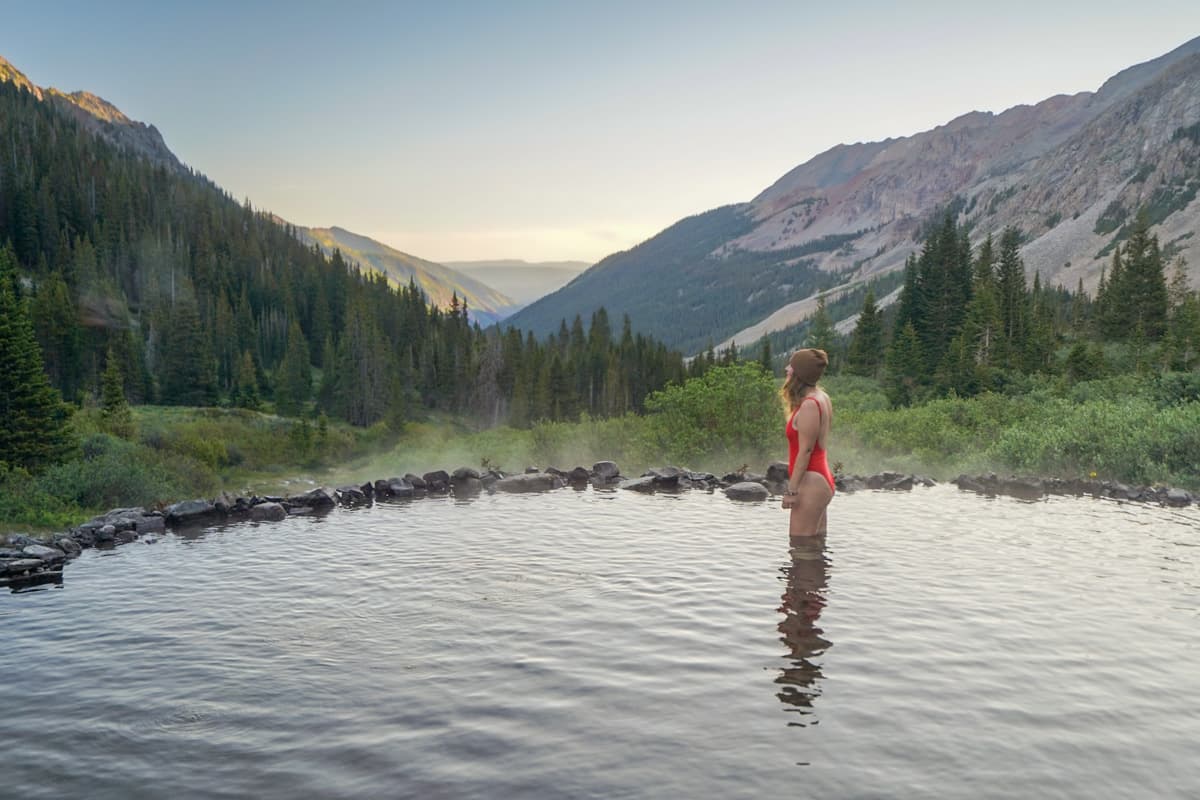 Woman standing in steamy Conundrum Hot Springs with mountains in the background in Maroon Bells-Snowass Wilderness in Aspen, Colorado