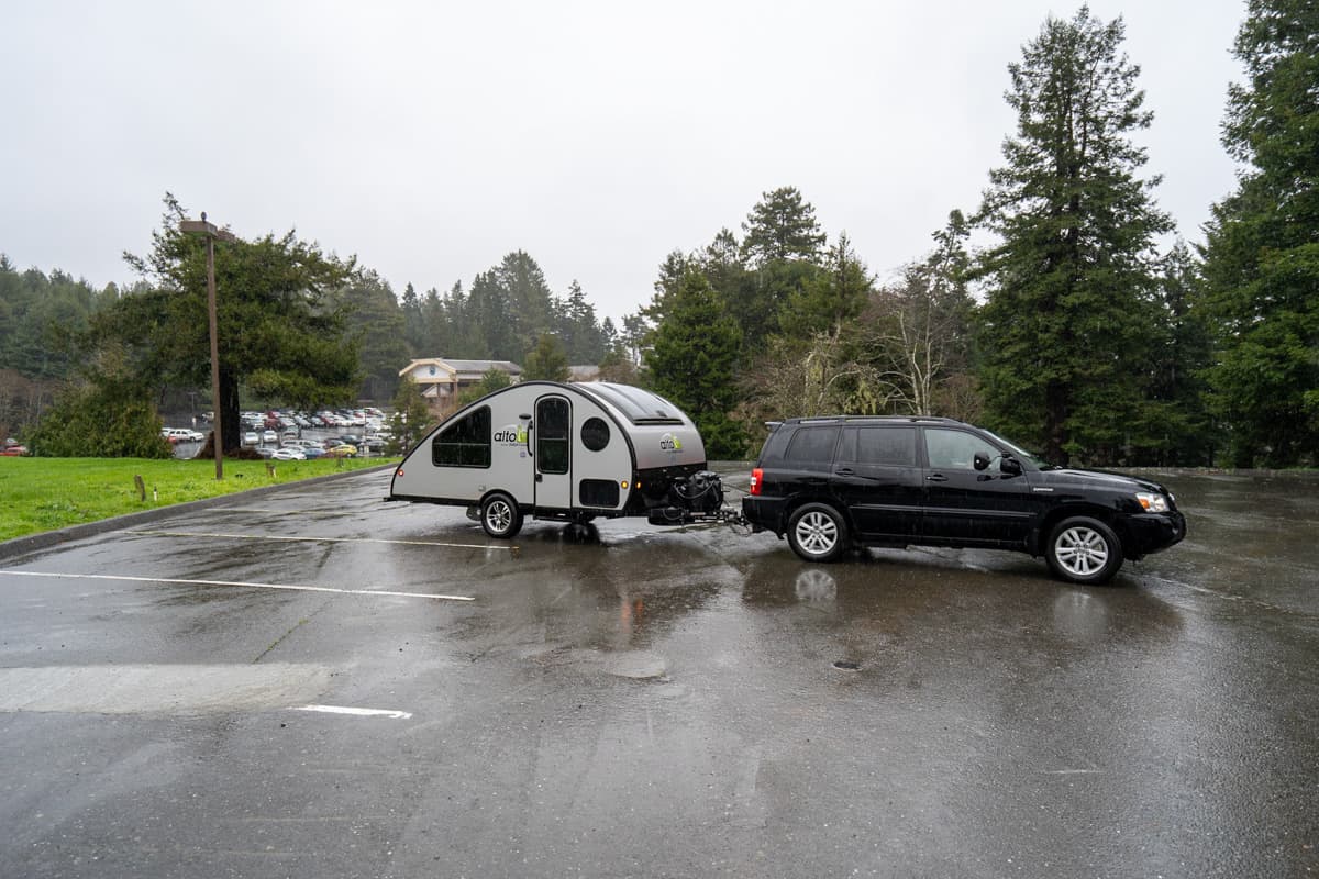 Black Highlander Hybrid SUV pulling a Safari Condo Alto R1723 in a rainy parking lot
