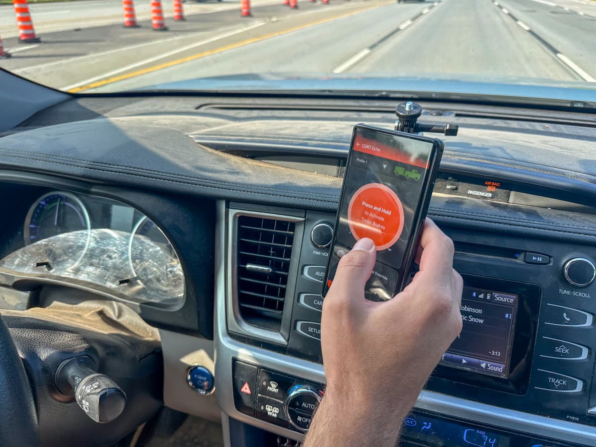 Close-up of man pressing the manual override button on the OneControl Auto application on a cell phone mounted to his dashboard while driving