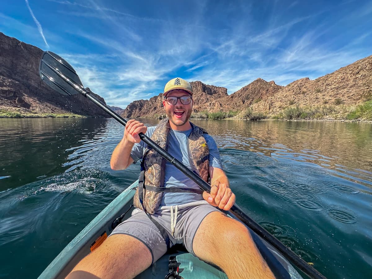 Man paddling in a kayak down the Colorado River with rock formations in the background in the Lake Mead National Recreation Area in Willow, Arizona