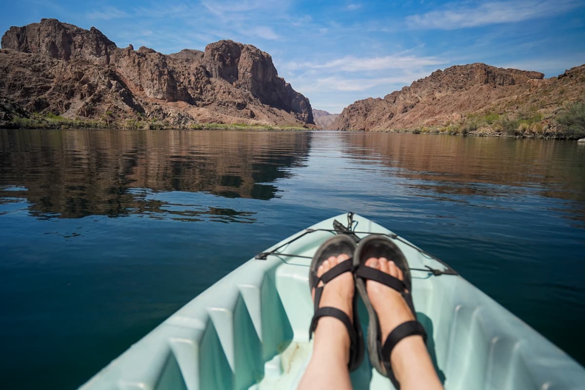 Woman's feet in the front of a kayak with the red rock canyons along the Colorado River in the background in Lake Mead National Recreation Area in Willow, Arizona