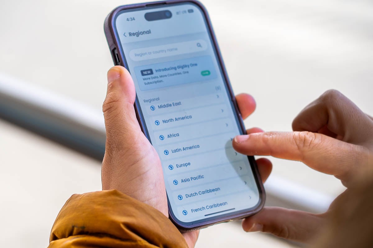 Woman holding a cell phone with different GigSky regional eSIM plans