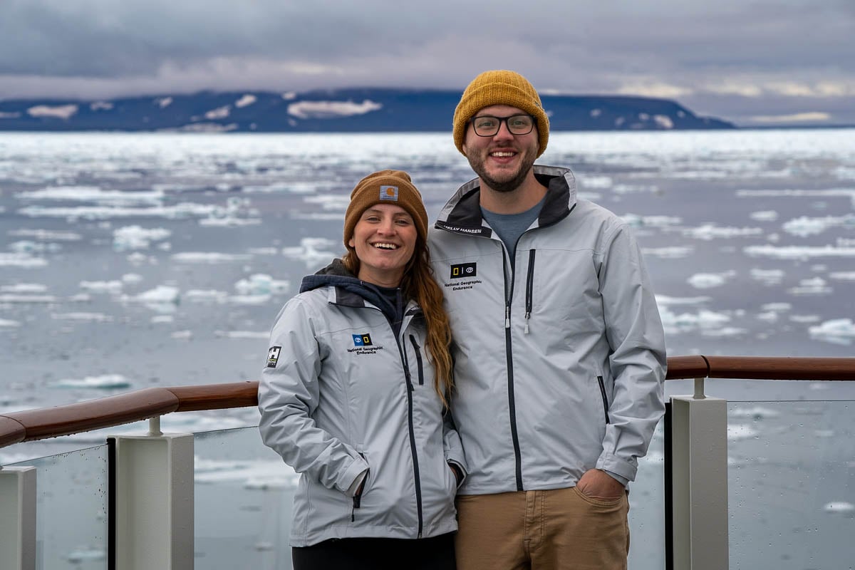 Smiling couple on the outer deck of National Geographic Endurance on a National Geographic-Lindblad Expeditions cruise with pack ice in the background in Greenland