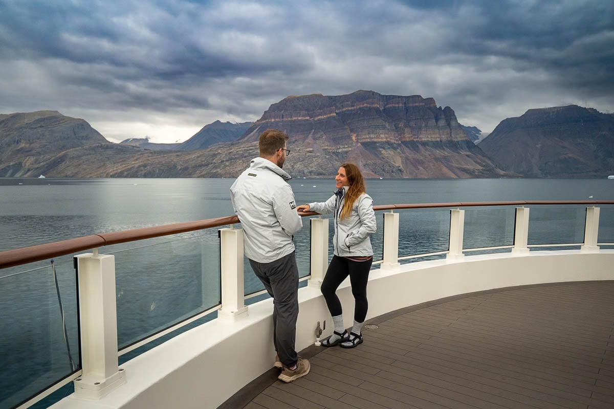 Smiling couple with rock formation in the background in a fjord on the National Geographic Endurance ship in Northeastern Greenland