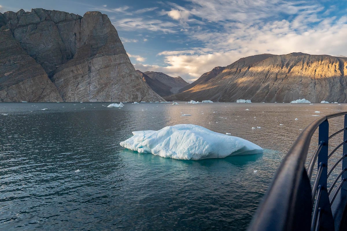 Iceberg with mountains painted with golden light from the outer deck of the National Geographic Endurance in Northeast Greenland National Park in Greenland