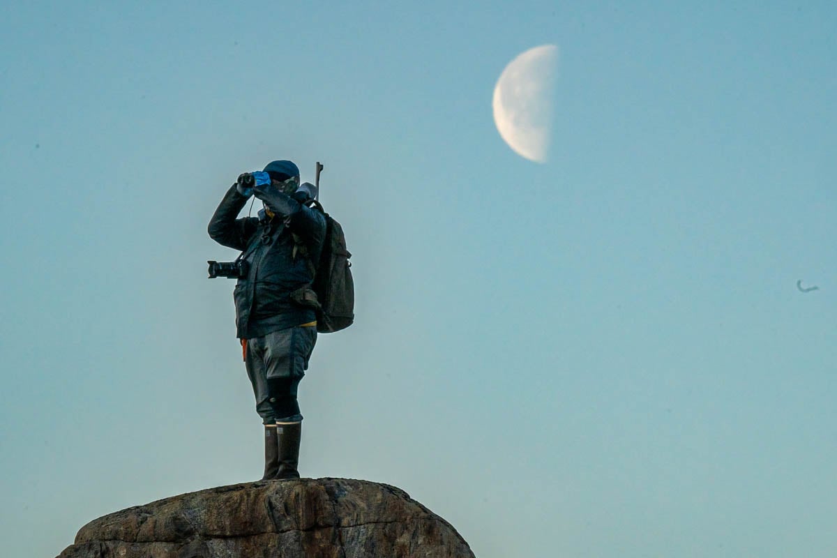 Expedition guide for National Geographic-Lindblad Expeditions looking through binoculars with a half moon in the background in Northeast Greenland National Park in Greenland