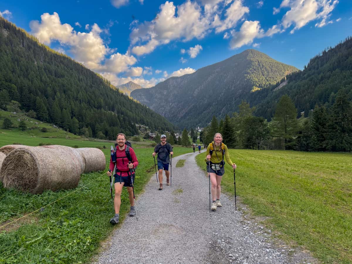 Three hikers walking along a gravel pathway with mountains in the background outside of Trient, Switzerland along the Tour du Mont Blanc