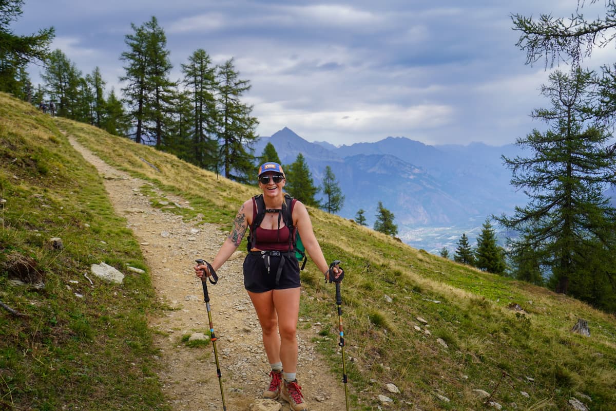 Smiling woman standing on a rocky path with the Bermese Alps in the background near Trient, Switzerland along the Tour du Mont Blanc