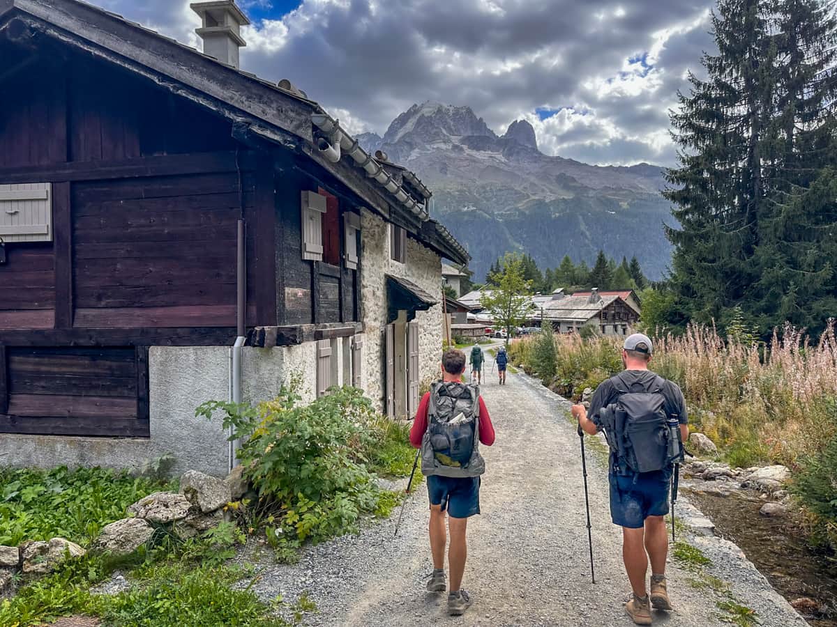 Two men hiking near a wooden chalet with Mont Blanc in the background along the Tour du Mont Blanc