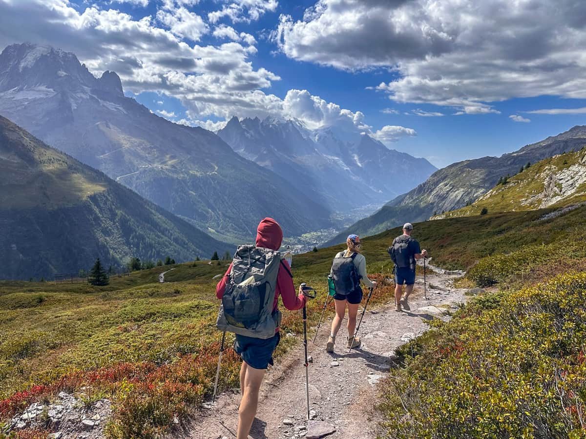 Three hikers walking along a dirt path with the Mont Blanc massif in the background near Chamonix, France along the Tour du Mont Blanc