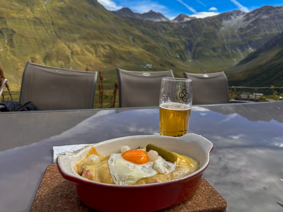 Dish of Swiss rosti with a glass of beer with the Swiss Alps in the background at Gîte Alpage de La Peule near La Fouly, Switzerland along the Tour du Mont Blanc