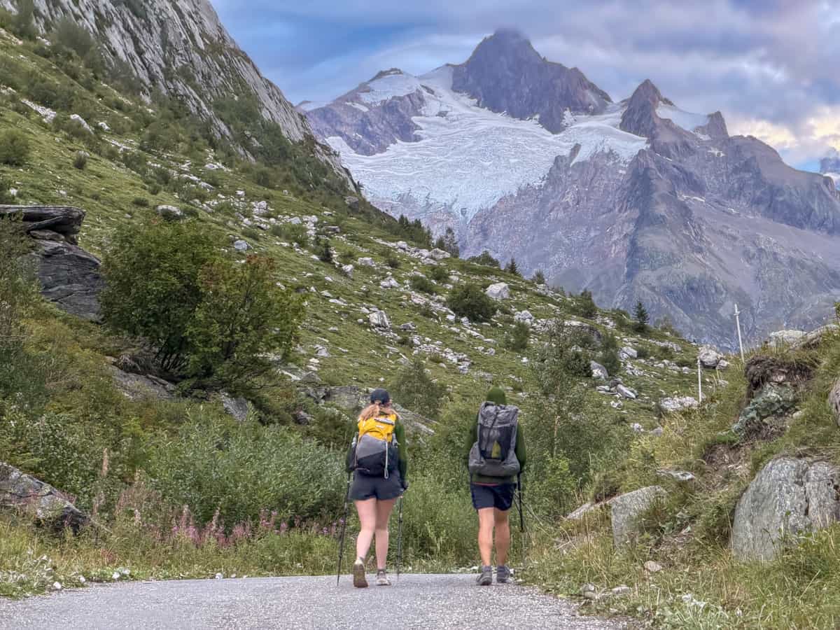 Couple hiking along a trail with a glaciated mountain in the background near Les Chapieux, France along the Tour du Mont Blanc