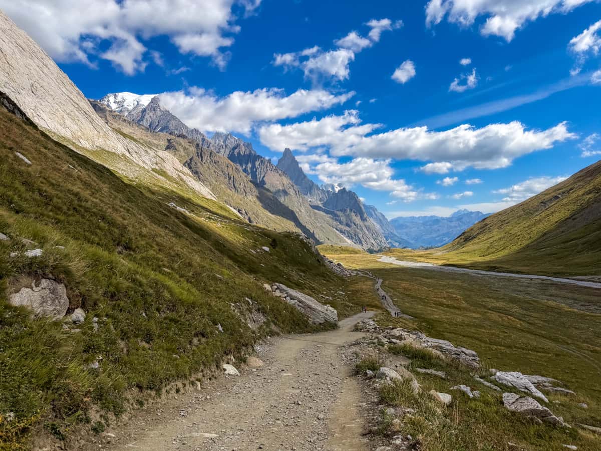 Rocky trail leading down a slope with jagged Italian Alps in the background at the Col de la Seigne pass along the Tour du Mont Blanc