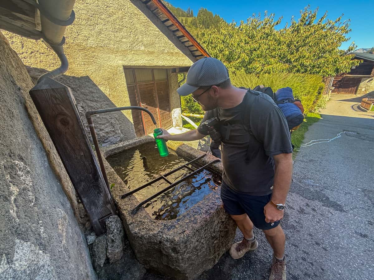 Man filling up a Nalgene bottle from a water fountain in Orsières, Switzerland along the Tour du Mont Blanc