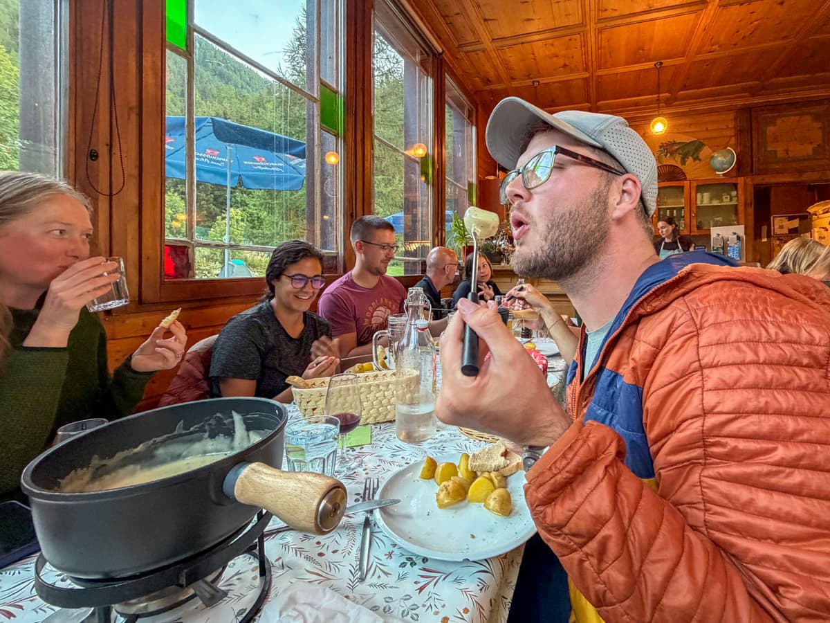 Man blowing on a potato on a fondue stick at a long table at Auberge Gîte Bon Abri in Champex-Lac, Switzerland in Tour du Mont Blanc