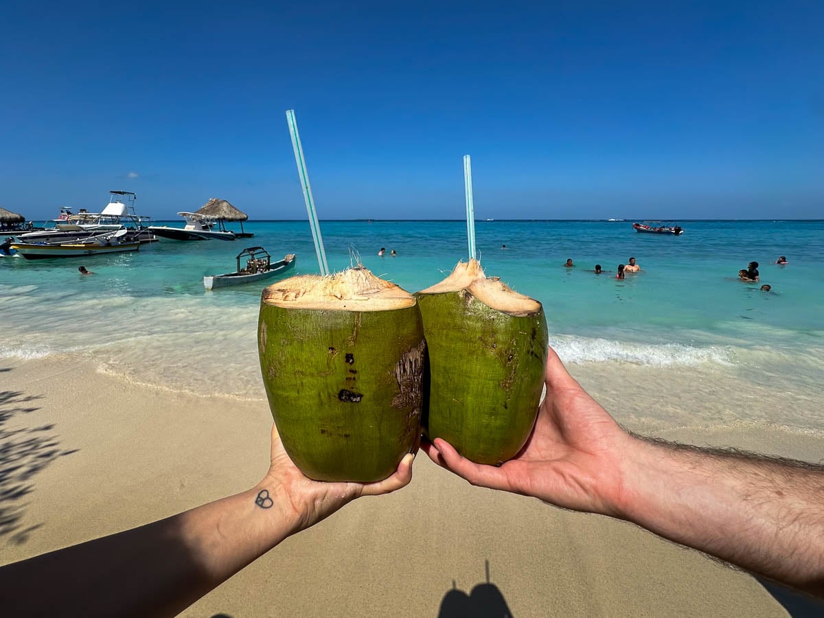 Couple cheersing fresh coconut with turquoise water at Playa Libre in the background in Isls Grande, Colombia