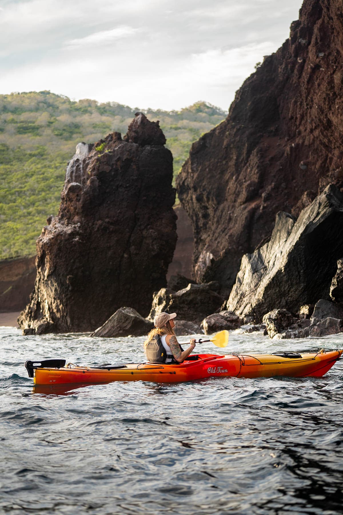 Woman kayaking along rocky cliffside in Isabela Island in the Galapagos Islands of Ecuador while cruising with National Geographic Lindblad Expeditions