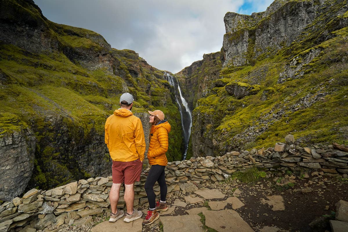 Couple standing on a cliff overlooking the Glymur Waterfall surrounded by mossy green cliffs in Iceland