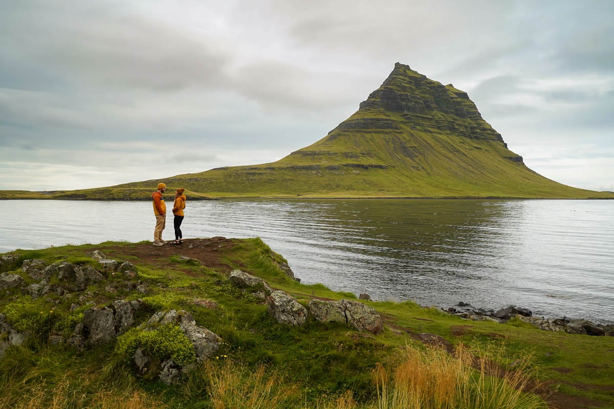 Couple standing on a rocky outcropping with Kirkufjell and a lake in the background in the Snaefelsness Peninsula of Iceland