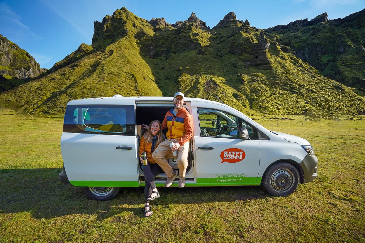 Couple sitting in the open door of a Happy Campers campervan at the Thakgil Campground in Iceland