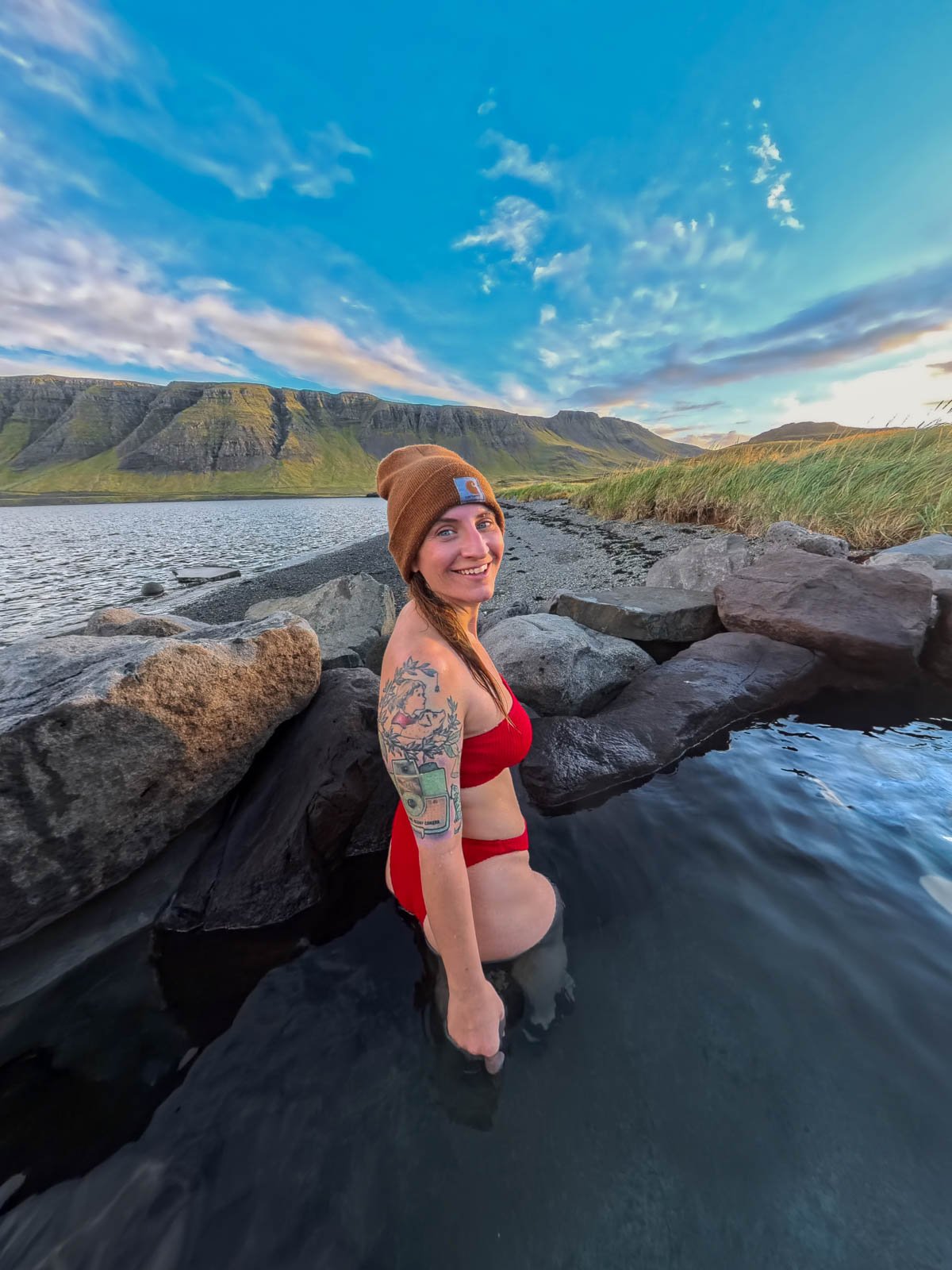 Woman smiling in a pool in Hvammsvik Hot Springs with a green mountain and fjord in the background in Iceland