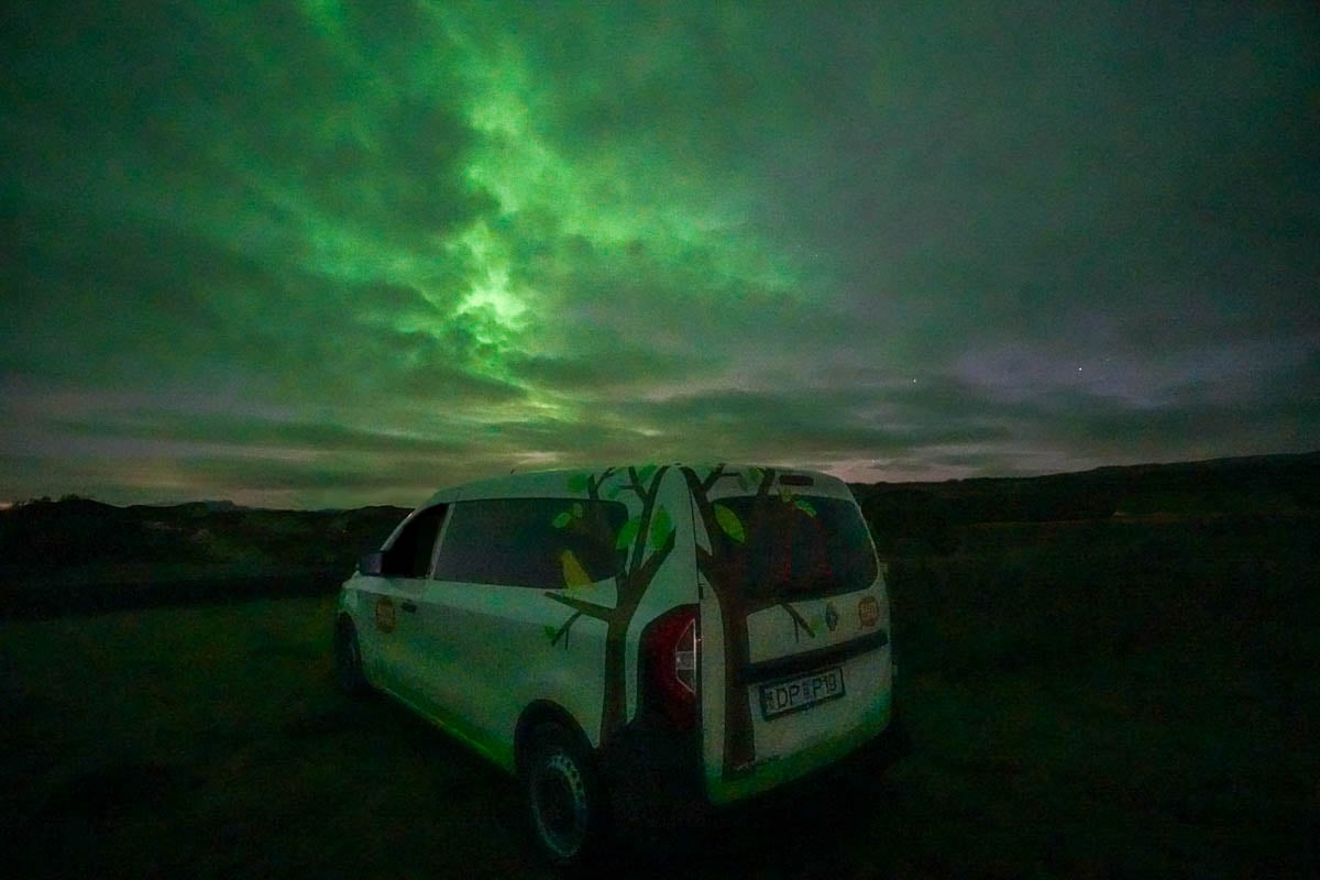 Campervan with the Northern Lights under clouds in Camp Thingvellir near Thingvellir National Park in Iceland
