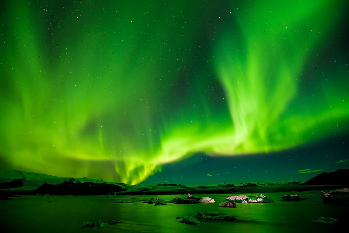 Northern Lights above the ocean and snow-capped mountains in Iceland