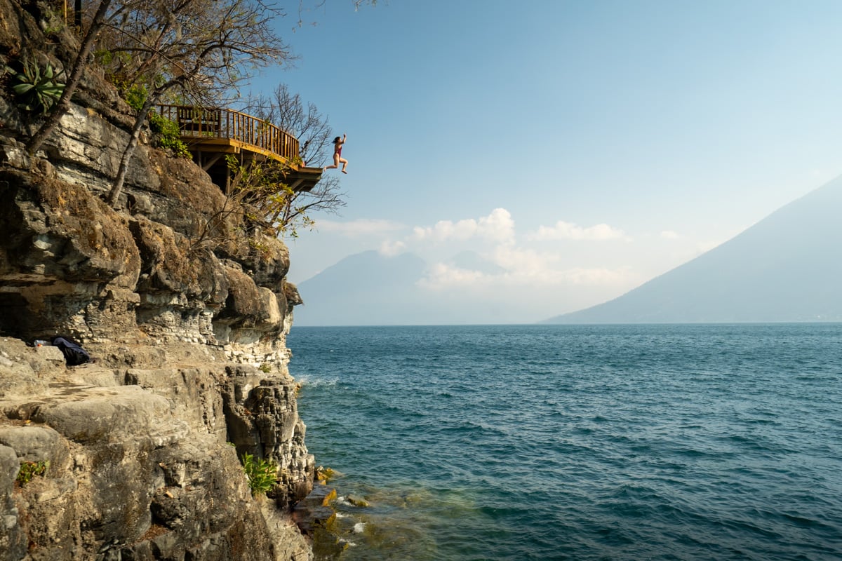Woman jumping off a wooden balcony from San Marcos into the water of Lake Atitlan in Guatemala