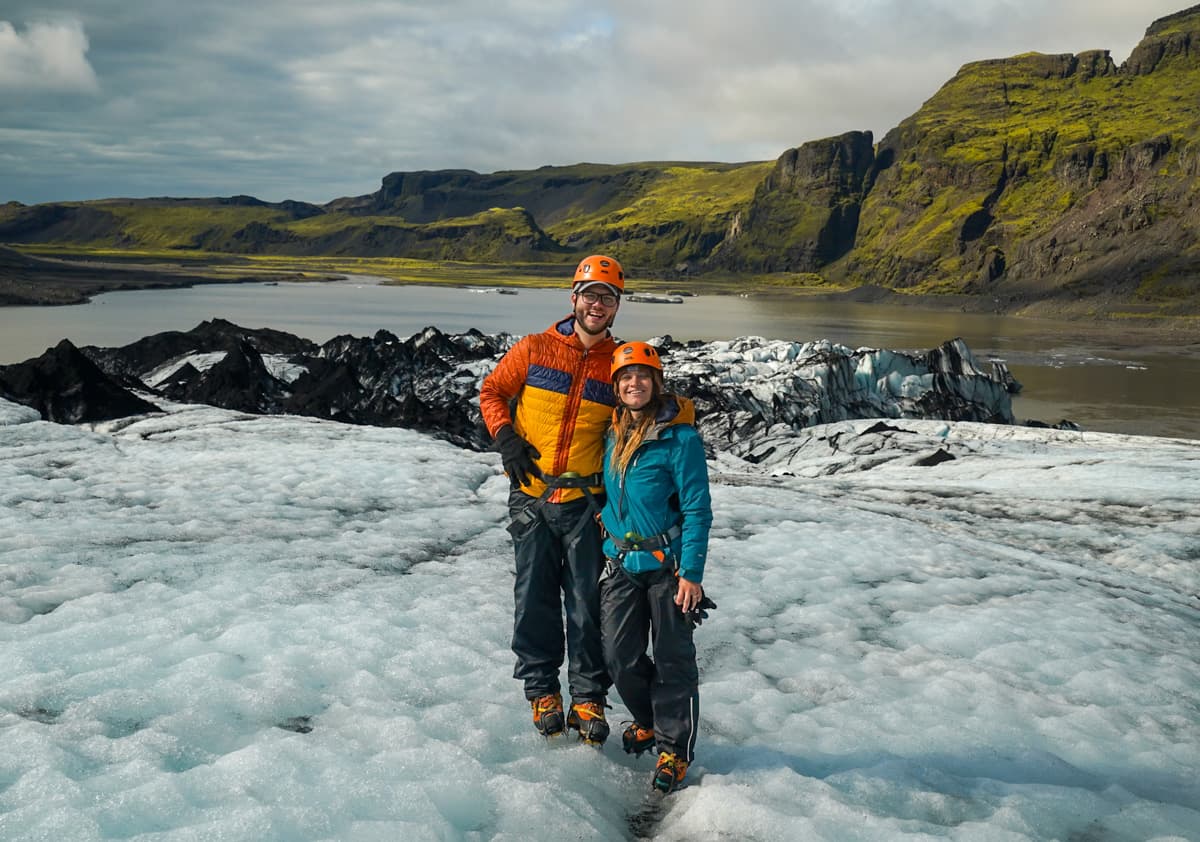 Smiling couple standing on a glacier with mossy mountains in the background in Iceland