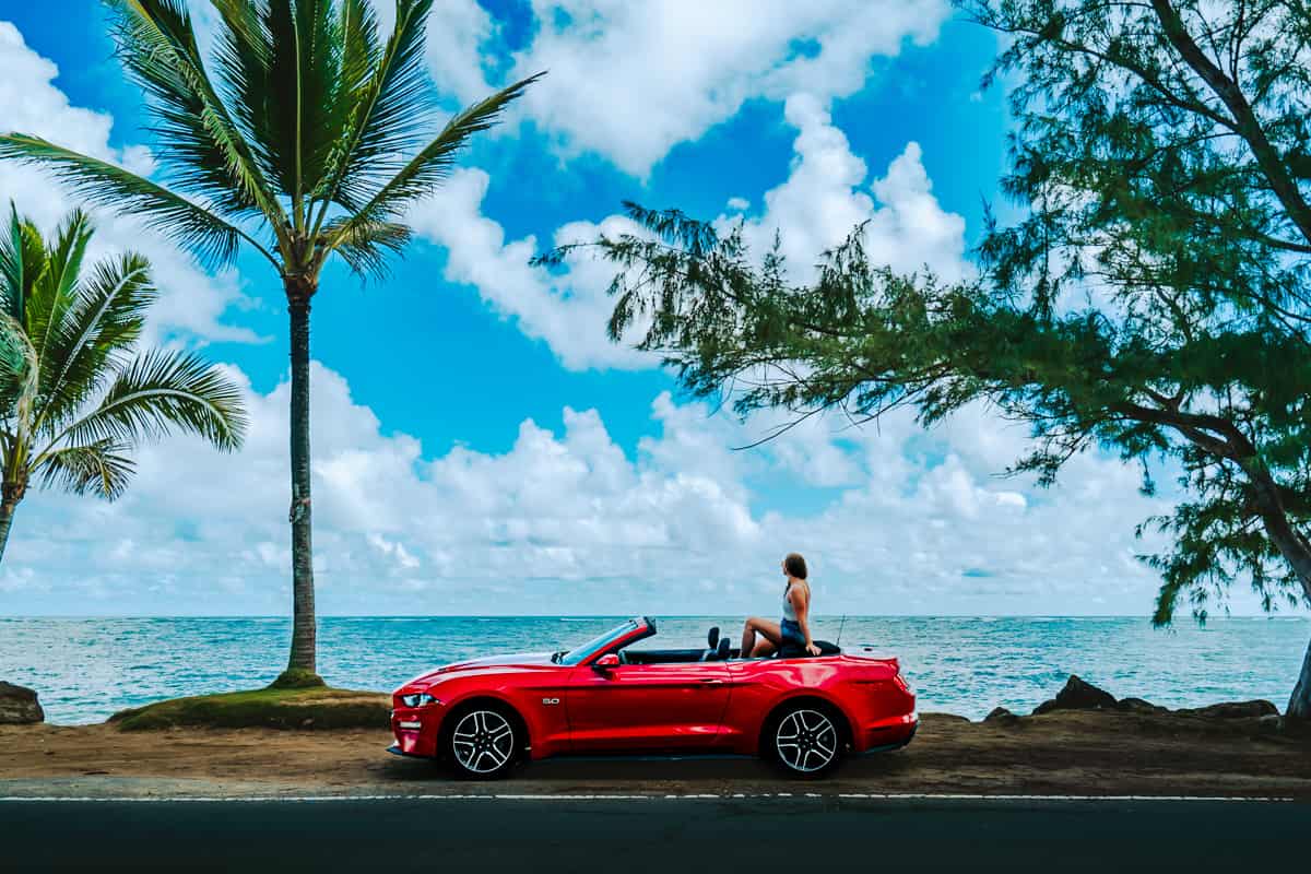 Woman sitting on top of a convertible Mustang along the North Shore of Oahu