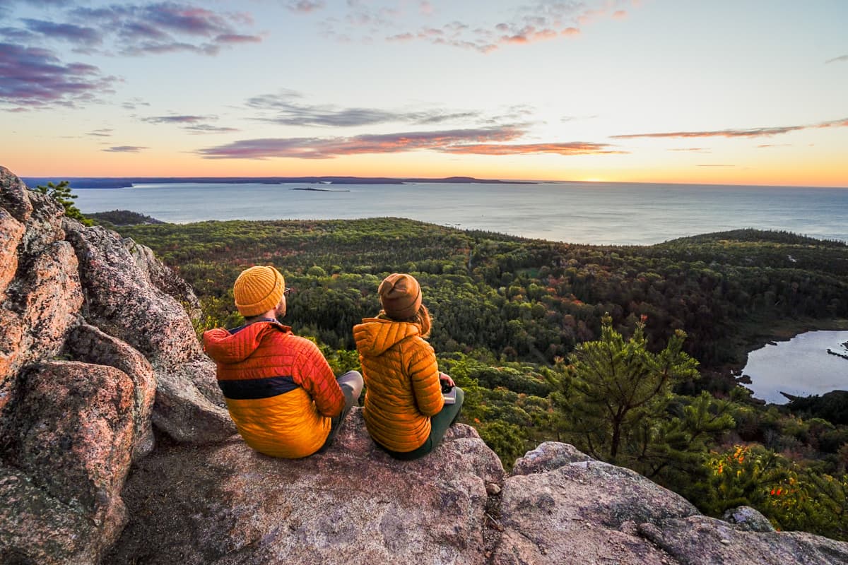 Couple sitting on a rock along the Beehive Trail at Acadia National Park watching the sunrise over the Atlantic Ocean