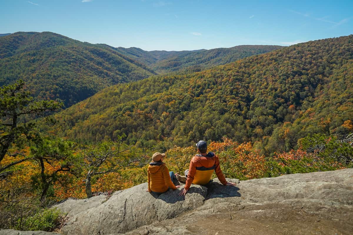 Couple sitting on a rock ledge along the Old Rag Trail overlooking mountains with fall foliage in October in Shenandoah National Park