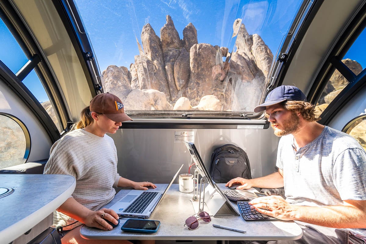 Couple working on their laptops in an RV with a rock formation out the window in the Alabama Hills, California