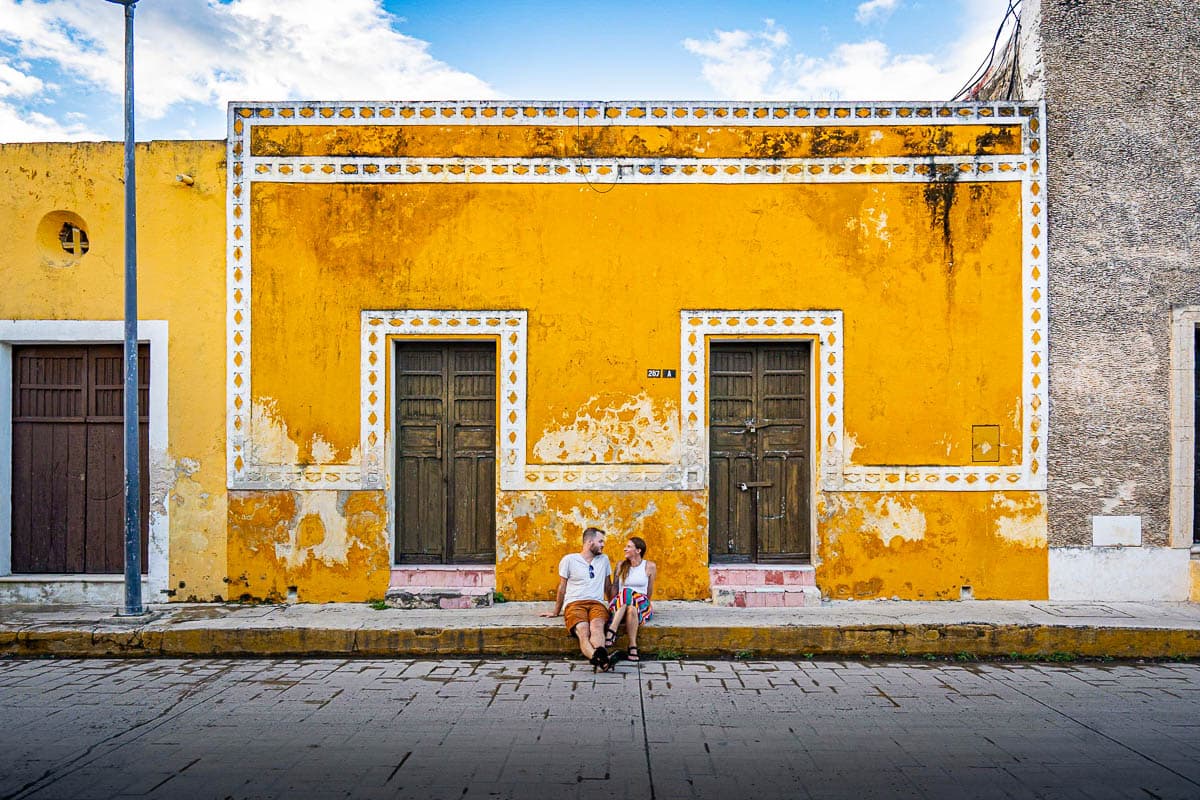 Couple sitting on a street curb in front of a colorful house in Izamal, Mexico