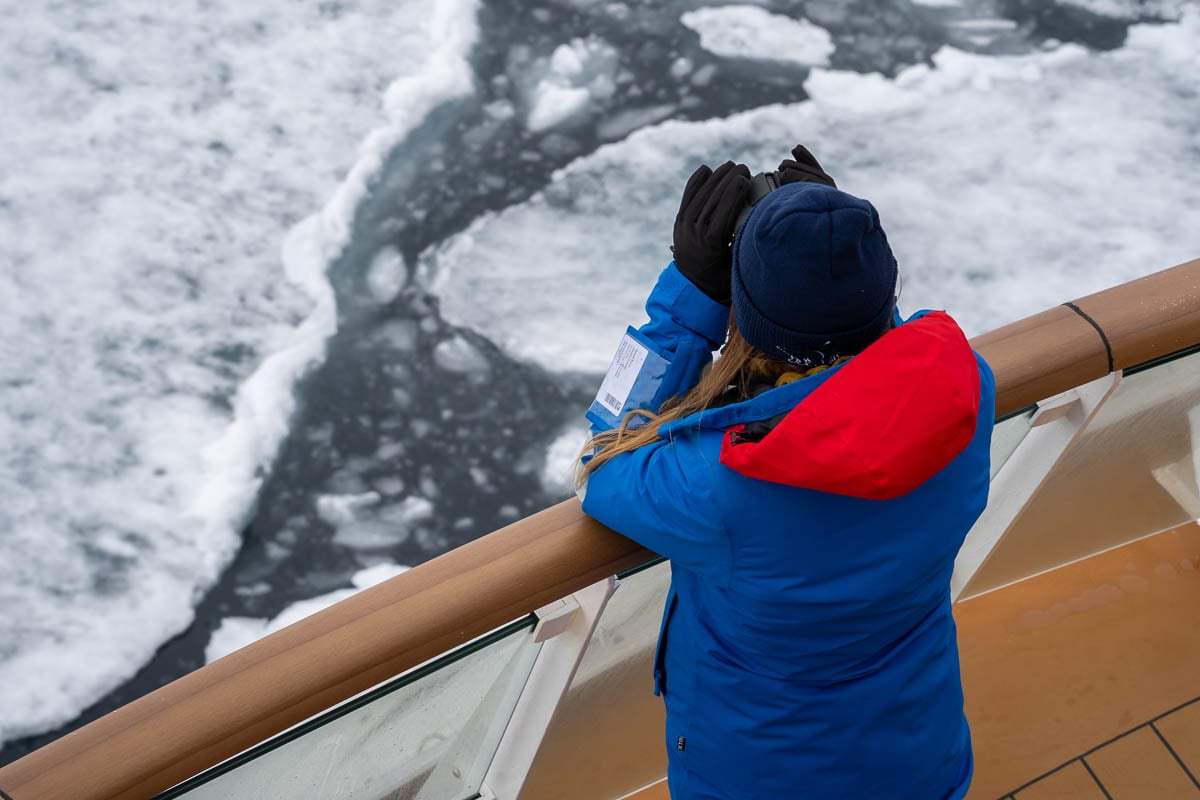 Woman looking through binoculars on the observation deck of a cruise ship with pack ice on the background in Svalbard, Norway