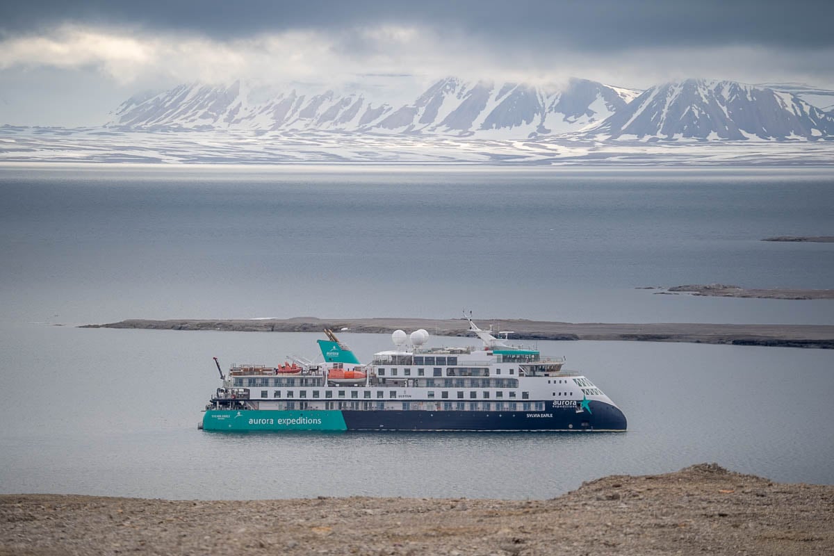 Aurora Expeditions Sylvia Earle cruise ship floating in front of misty mountains in the background in Svalbard, Norway