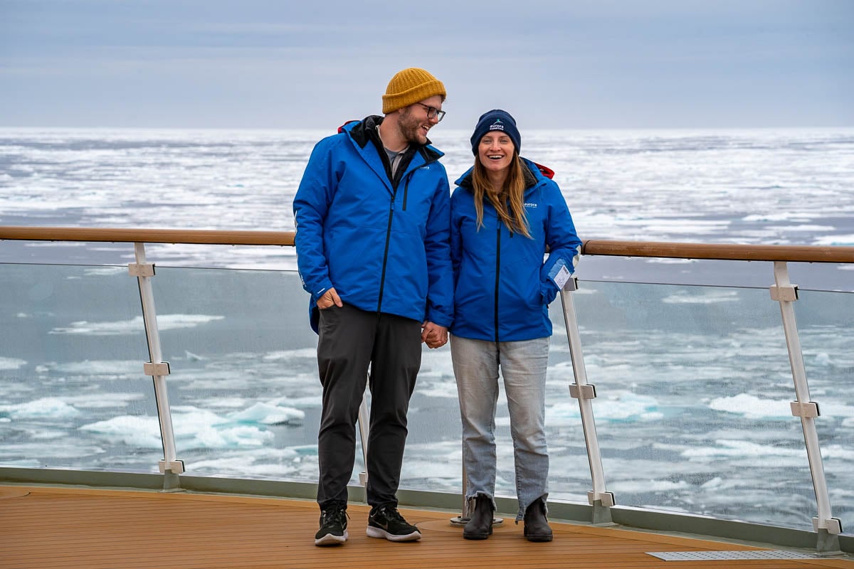 Couple holding hands on the Observation Deck of Aurora Expedition's Sylvia Earle cruise ship with pack ice in the background in Svalbard, Norway
