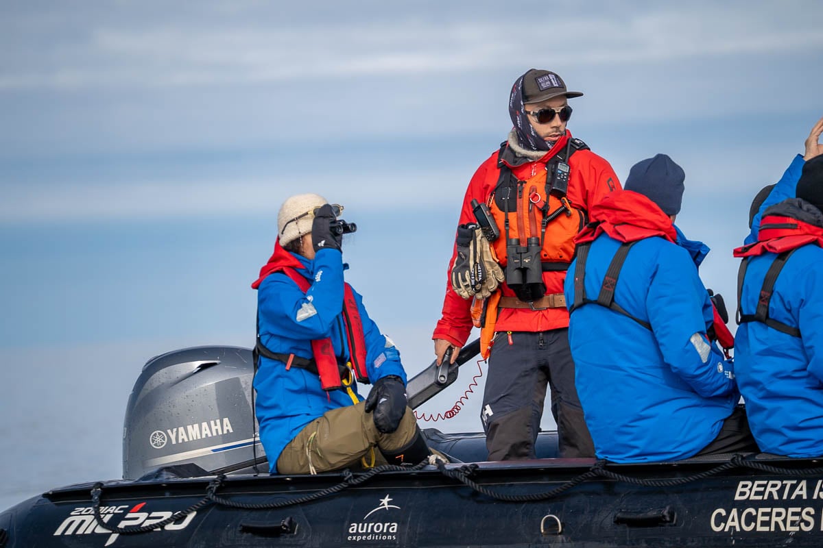 Woman with binoculars sitting on a Zodiac boat with an expedition guide steering the boat in Svalbard, Norway