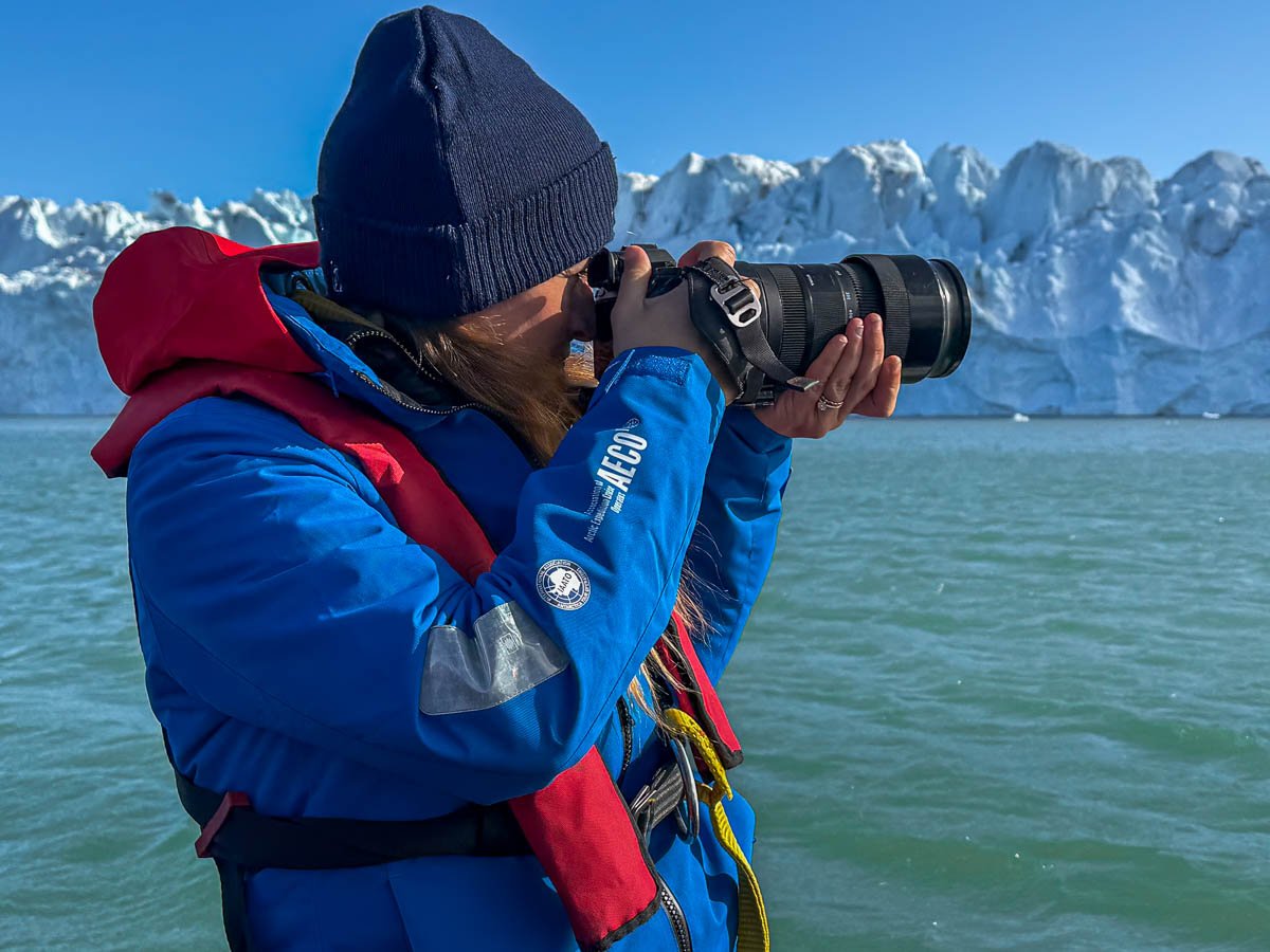 Woman with a long lens on a camera with a large glacier in the background in Svalbard, Norway