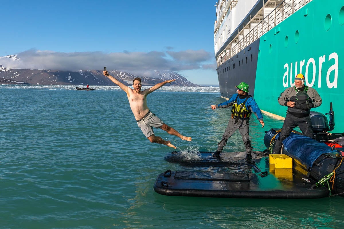 Man jumping off a platform with mountains and icebergs in the background on a Svalbard cruise