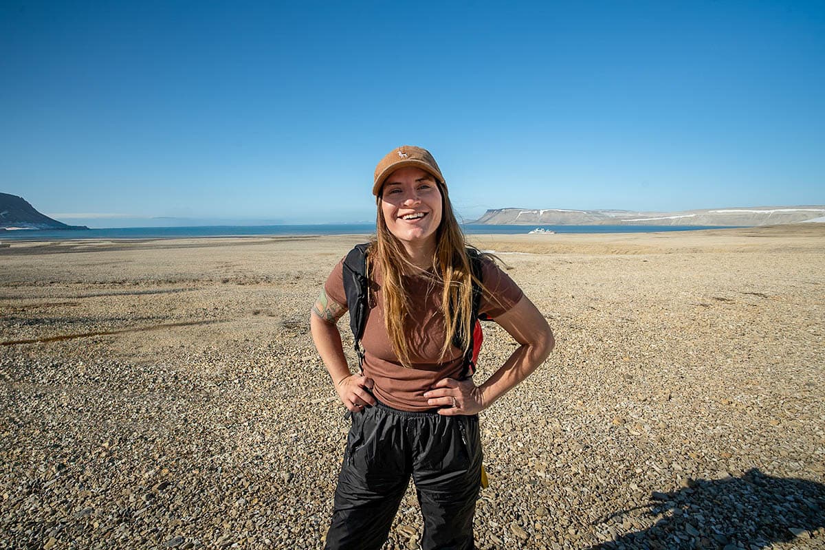Smiling woman on a rocky beach with mountains in the background in Svalbard, Norway
