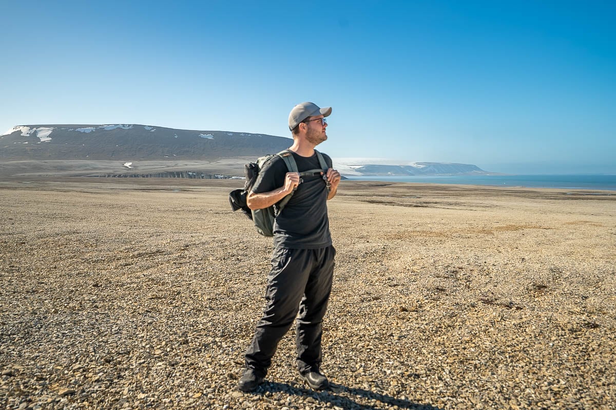 Man standing on rocky slope with mountain in the background in Svalbard, Norway